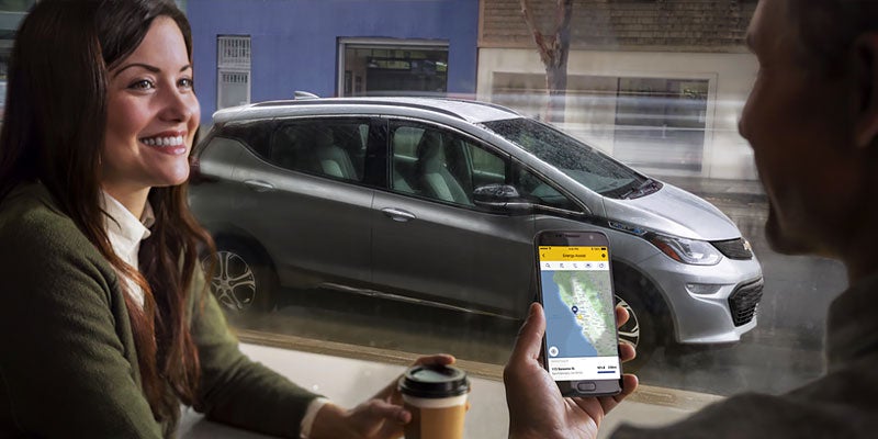 man holding phone and woman holding coffee seating in a cafe and Chevrolet Bolt EV parked outside
